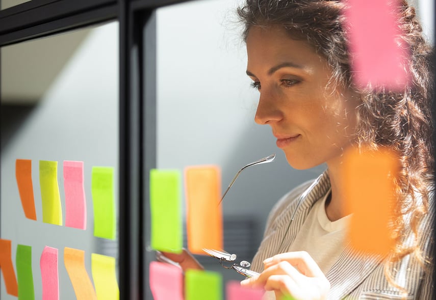 Eine Beraterin der contec GmbH Unternehmensberatung und Personalberatung der Gesundheitswirtschaft und Sozialwirtschaft für den Fachbereich Komplexträger stehen vor einer Scheibe auf der mehrere Post-It kleben