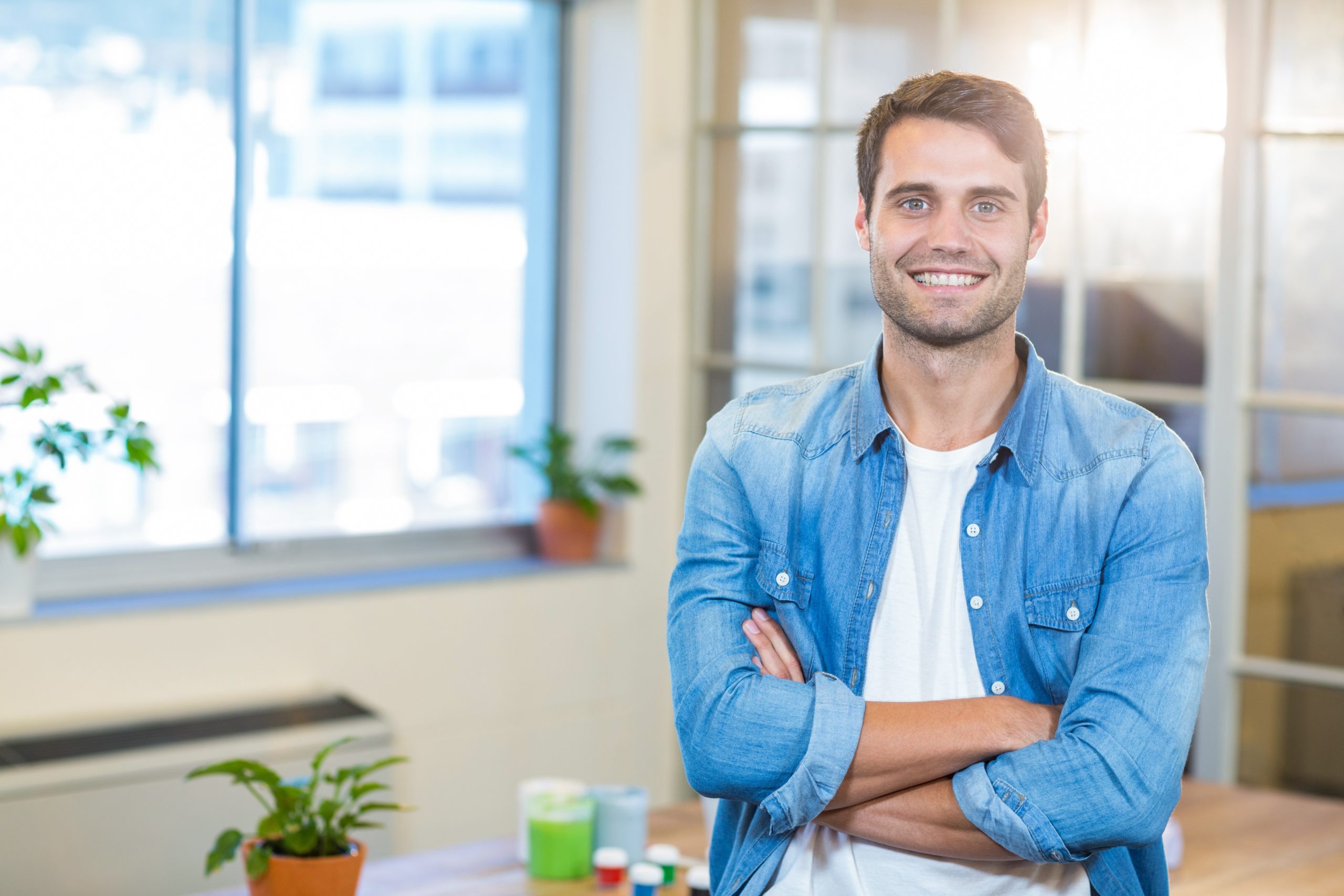Ein Wohnbereichsleiter steht mit verschränkten Armen in einem Büro und lächelt in die Kamera.