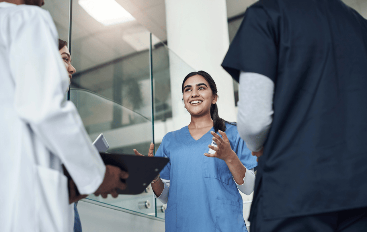 Pflegepersonal und Ärzte im Gespräch zur PPR 2.0. Im Fokus steht eine Frau in blauem Kasack.
